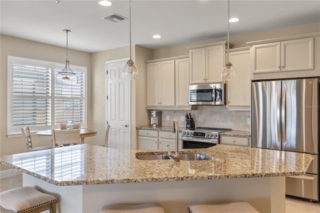 kitchen with stainless steel appliances, pendant lighting, sink, and a center island with sink