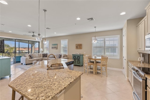 kitchen with sink, light stone counters, hanging light fixtures, stainless steel appliances, and a kitchen island with sink