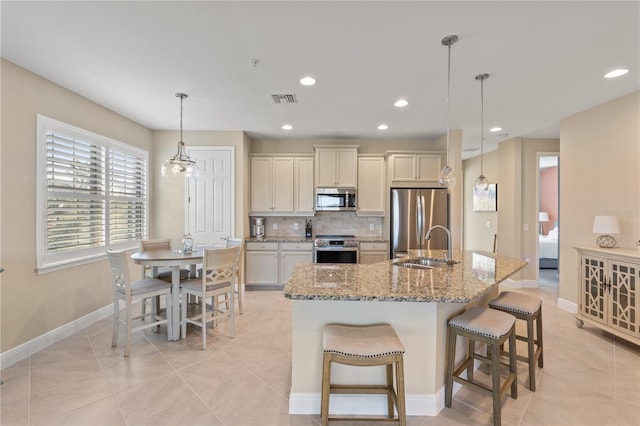 kitchen with pendant lighting, an island with sink, a kitchen breakfast bar, stainless steel appliances, and light stone countertops