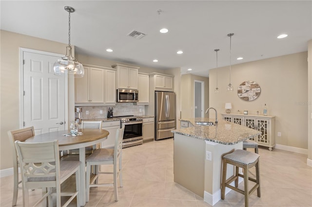 kitchen featuring sink, light stone counters, a center island with sink, pendant lighting, and stainless steel appliances