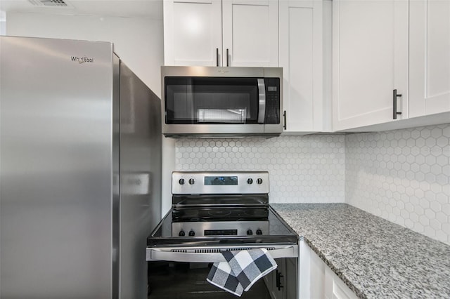 kitchen featuring white cabinetry, stainless steel appliances, light stone countertops, and backsplash