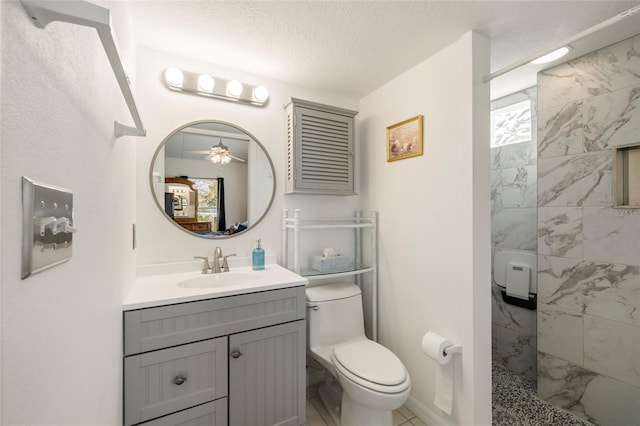 bathroom featuring ceiling fan, tiled shower, vanity, a textured ceiling, and toilet