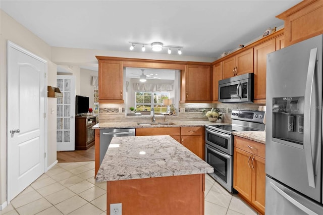 kitchen featuring sink, a kitchen island, stainless steel appliances, light stone countertops, and light tile patterned flooring