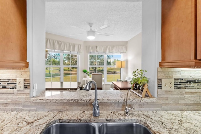 kitchen with light stone counters, ceiling fan, sink, and backsplash