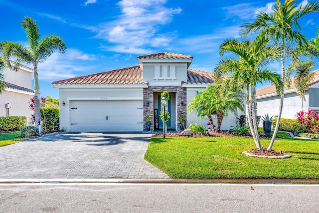 mediterranean / spanish-style house featuring an attached garage, stone siding, decorative driveway, stucco siding, and a front yard