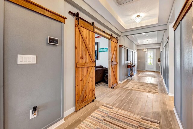 hall with wood tiled floor, baseboards, a tray ceiling, and a barn door