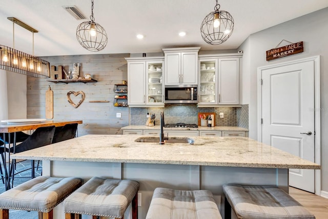 kitchen with glass insert cabinets, pendant lighting, stainless steel microwave, and a kitchen breakfast bar