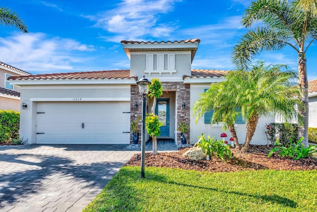 mediterranean / spanish-style home with decorative driveway, stucco siding, an attached garage, stone siding, and a front lawn