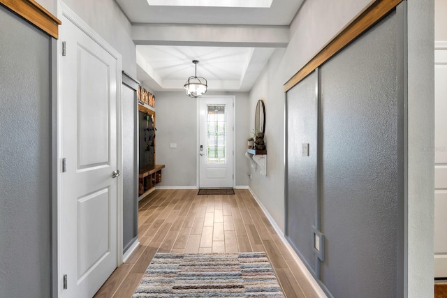 entryway featuring wood tiled floor, a tray ceiling, a chandelier, and baseboards