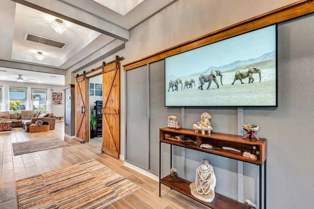 hallway with a barn door, wood finish floors, visible vents, baseboards, and a raised ceiling