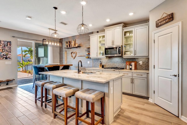 kitchen with stainless steel appliances, a sink, a kitchen breakfast bar, an island with sink, and glass insert cabinets