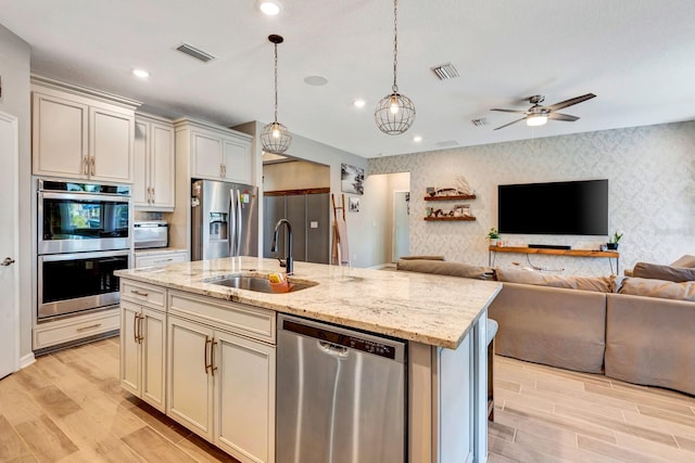 kitchen with wallpapered walls, a center island with sink, visible vents, stainless steel appliances, and a sink