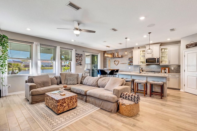 living room with light wood-style floors, visible vents, and ceiling fan