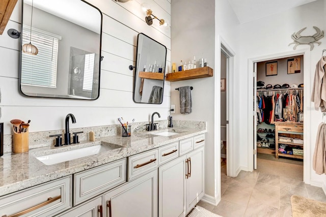 full bath with double vanity, a walk in closet, a sink, and tile patterned floors