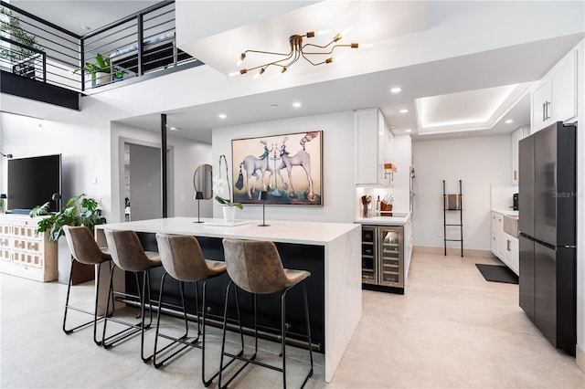 kitchen featuring white cabinetry, black refrigerator, beverage cooler, and a center island with sink