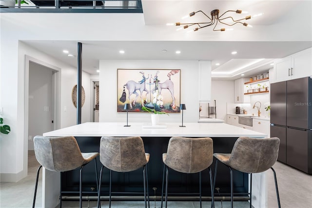 kitchen with light countertops, white cabinets, an island with sink, stainless steel fridge, and a kitchen bar