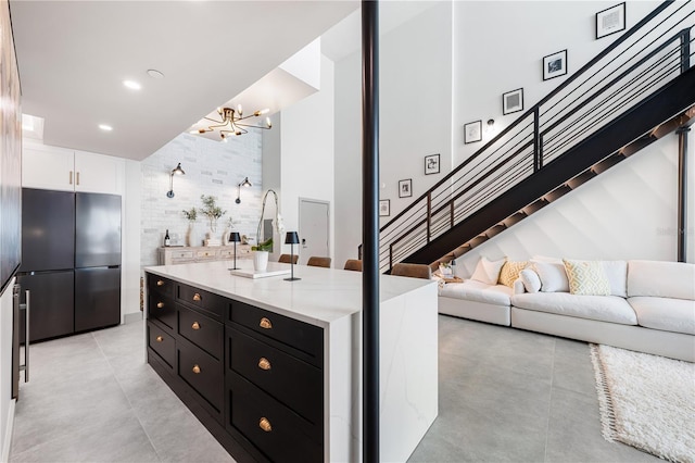 kitchen with light tile patterned floors, a kitchen island with sink, white cabinets, black fridge, and a chandelier