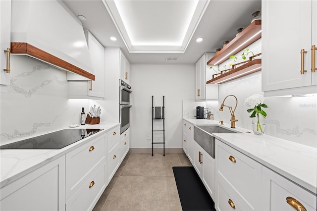 kitchen featuring black electric stovetop, open shelves, custom range hood, white cabinetry, and a sink