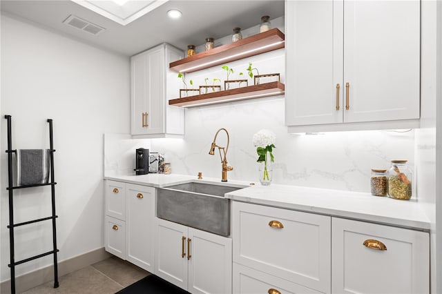 kitchen with sink, light tile patterned floors, white cabinetry, backsplash, and light stone counters