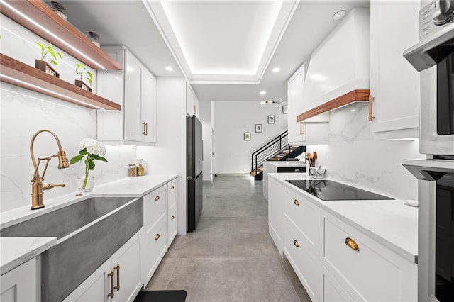 kitchen featuring white cabinetry, premium range hood, sink, and black appliances