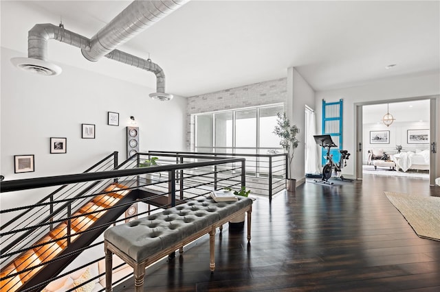 interior space with dark wood-type flooring, brick wall, visible vents, and an upstairs landing