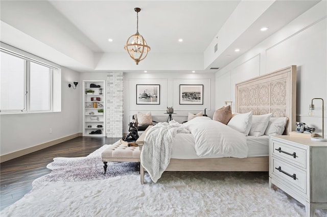 bedroom with dark hardwood / wood-style flooring, a raised ceiling, and an inviting chandelier