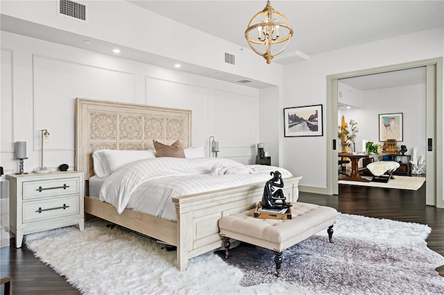 bedroom featuring dark wood-type flooring, visible vents, a decorative wall, and a notable chandelier