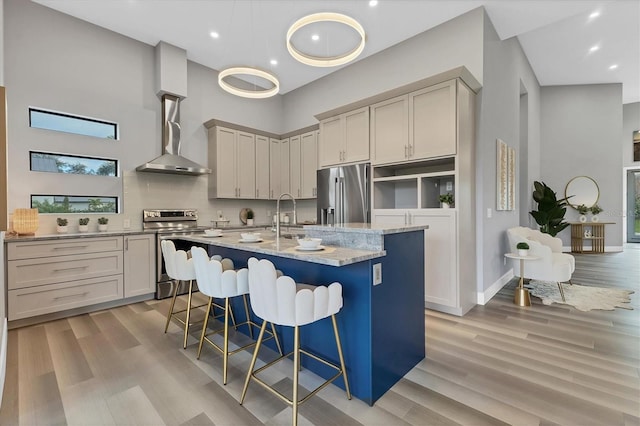 kitchen with appliances with stainless steel finishes, a breakfast bar, a high ceiling, a kitchen island with sink, and light stone countertops