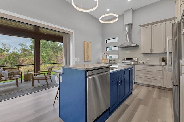 kitchen with wall chimney exhaust hood, appliances with stainless steel finishes, an island with sink, and white cabinets