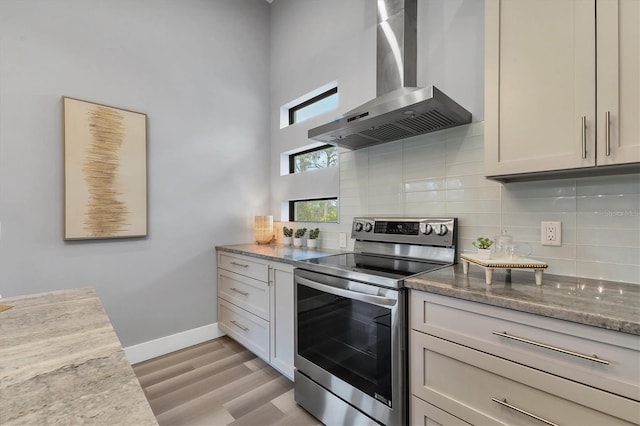 kitchen with light stone counters, electric range, light wood-type flooring, decorative backsplash, and wall chimney range hood