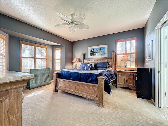 bedroom with ceiling fan, light colored carpet, and a textured ceiling