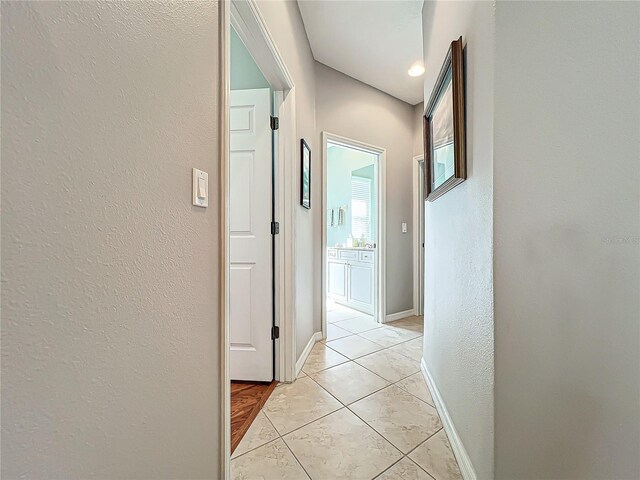 corridor featuring light tile patterned flooring, a textured wall, and baseboards