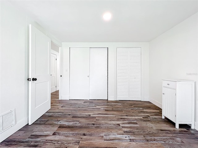 unfurnished bedroom featuring dark hardwood / wood-style flooring and two closets