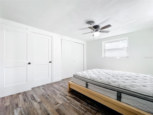 bedroom featuring hardwood / wood-style flooring, ceiling fan, and multiple closets