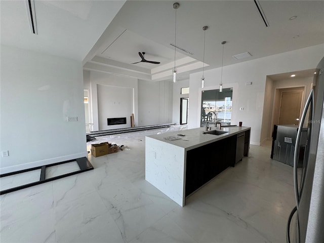 kitchen with sink, decorative light fixtures, a raised ceiling, ceiling fan, and a kitchen island with sink