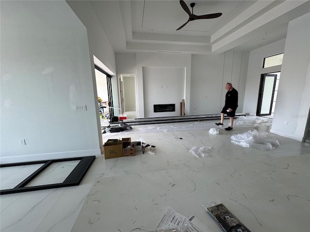 unfurnished living room with a fireplace, a raised ceiling, and ceiling fan