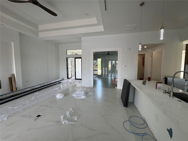 kitchen featuring sink, hanging light fixtures, ceiling fan, light stone counters, and a raised ceiling