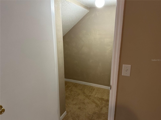 hall featuring carpet flooring, baseboards, vaulted ceiling, and a textured ceiling