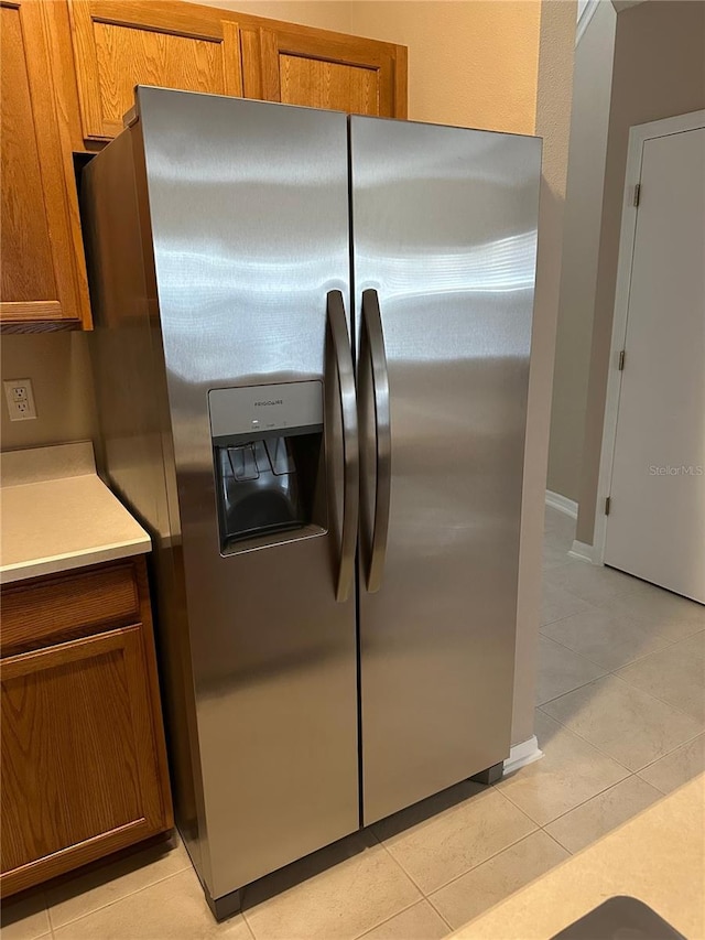kitchen with stainless steel refrigerator with ice dispenser, brown cabinetry, light tile patterned floors, and light countertops