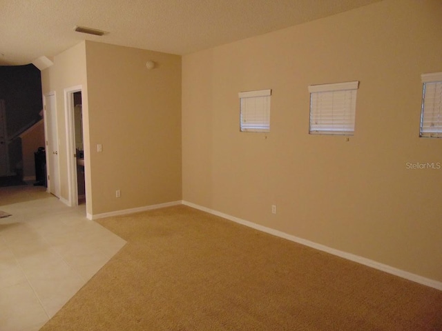 unfurnished room featuring light colored carpet, baseboards, a textured ceiling, and light tile patterned floors