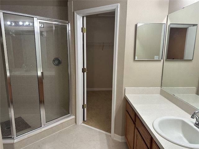 bathroom featuring a shower stall, vanity, a spacious closet, tile patterned floors, and baseboards