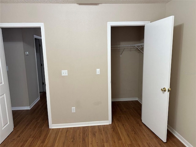 unfurnished bedroom featuring wood finished floors, baseboards, a closet, and a spacious closet