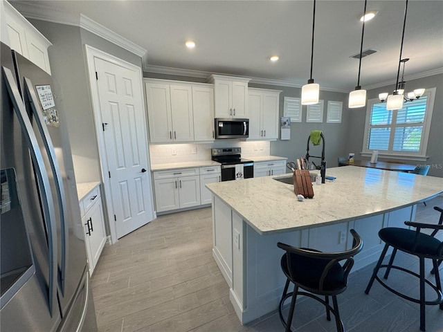 kitchen featuring appliances with stainless steel finishes, white cabinetry, an island with sink, hanging light fixtures, and light stone counters