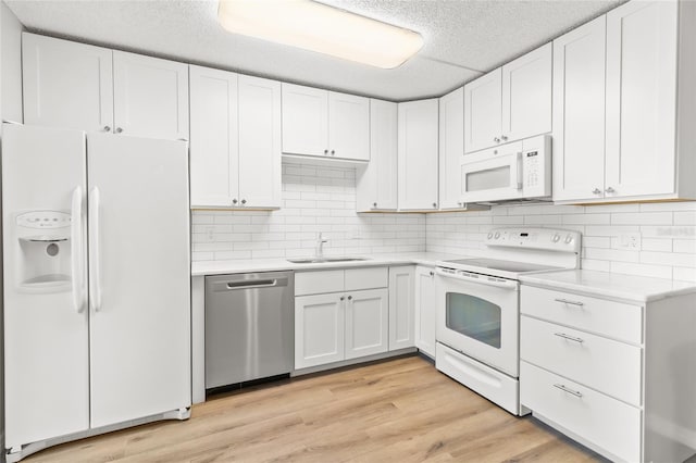 kitchen featuring sink, white cabinetry, light hardwood / wood-style flooring, white appliances, and backsplash