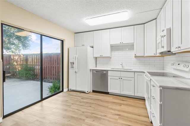 kitchen with sink, white appliances, white cabinetry, tasteful backsplash, and light wood-type flooring