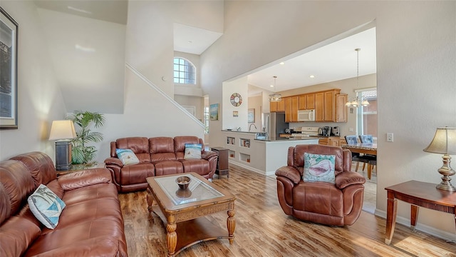 living room featuring a notable chandelier, a towering ceiling, and light hardwood / wood-style flooring