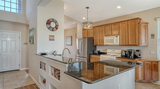 kitchen with light tile patterned floors, white appliances, sink, dark stone countertops, and hanging light fixtures