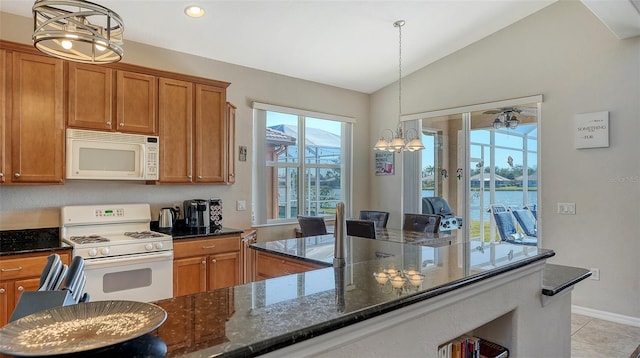 kitchen featuring a water view, vaulted ceiling, dark stone countertops, a notable chandelier, and white appliances