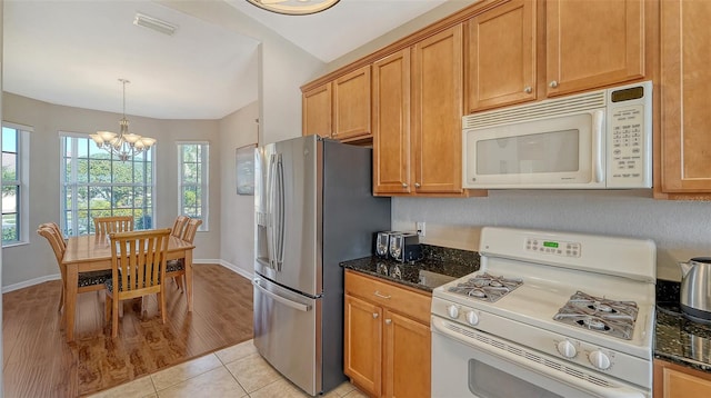 kitchen featuring light tile patterned flooring, an inviting chandelier, hanging light fixtures, dark stone countertops, and white appliances