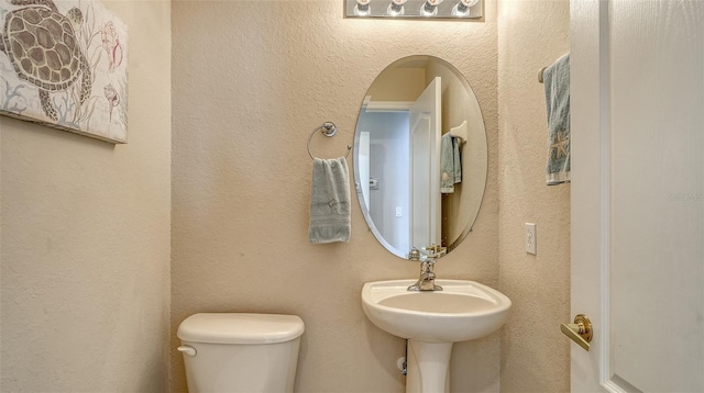 half bath featuring toilet and a textured wall